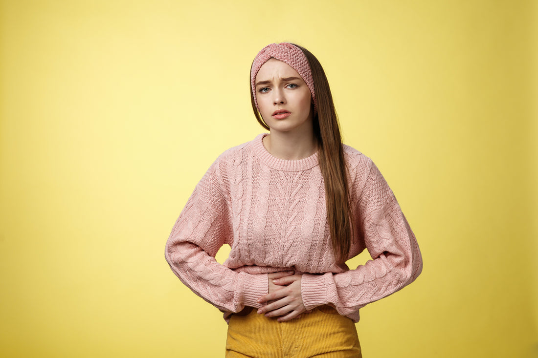 femme qui se tient le ventre avec les mains pour signaler une crampe dans le ventre et douleurs